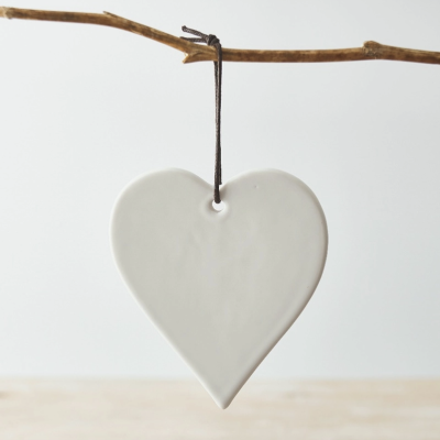Pingente cerâmico branco em forma de coração pendurado por cordão preto numa rama seca