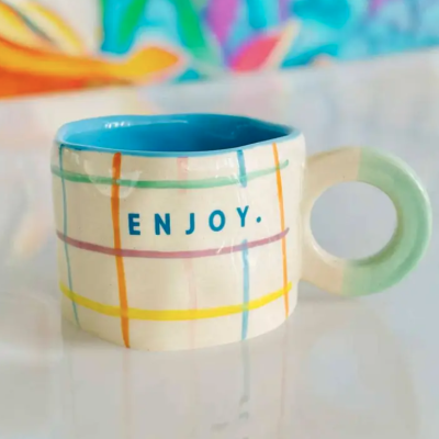 Caneca de cerâmica com interior azul e padrão colorido com a palavra ENJOY.