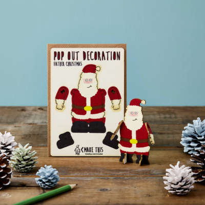 Decoração pop-out de Pai Natal em madeira com embalagem e pinhas coloridas sobre mesa de madeira