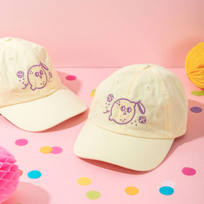 Bonés amarelos claros com bordado roxo de limão e flores sobre superfície rosa com confetes