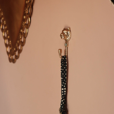 Gancho de parede dourado com cabeça de leão a segurar fita preta com bolinhas brancas