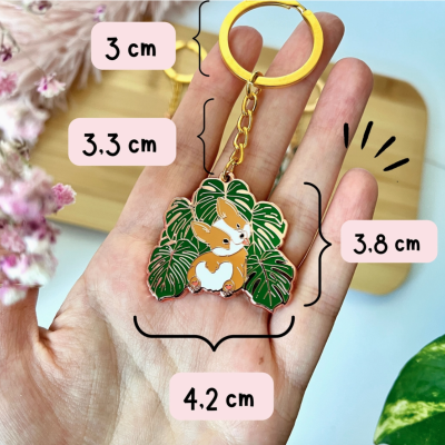Chaveiro dourado com pendente de cão Corgi entre folhas verdes tropicais