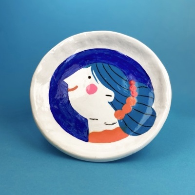 Prato cerâmico decorado com rosto feminino estilizado em azul, branco e cor-de-laranja