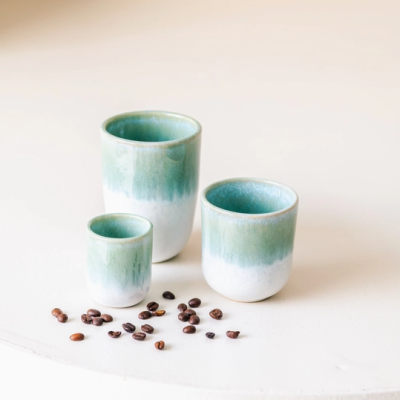 Conjunto de três copos cerâmicos verde e branco com grãos de café à frente