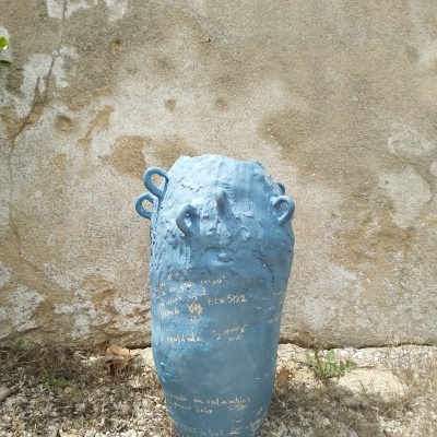 Vaso de cerâmica azul com inscrições brancas e três alças em fundo de parede bege