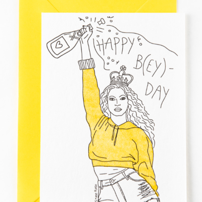 Cartão com ilustração mulher de blusão amarelo a brindar e texto 'HAPPY B(EY)-DAY'