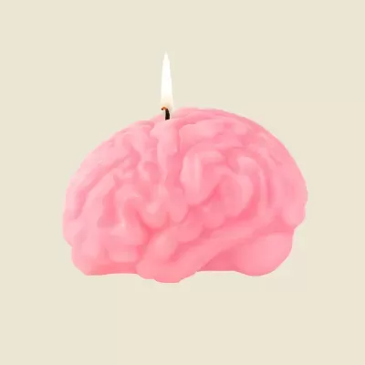 Vela rosa em forma de cérebro acesa sobre fundo bege claro