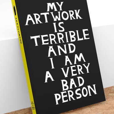 Caderno de desenho preto com texto branco e lombada amarela sobre superfície de madeira