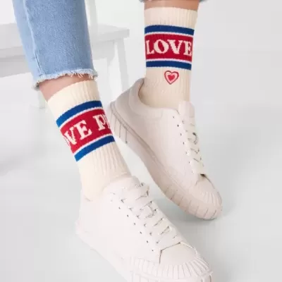 Meias bege com texto LOVE e WE, calças ganga e ténis brancos.