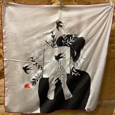 Lenço branco com desenho artístico em preto, branco e vermelho de mulher com livro e elementos naturais.