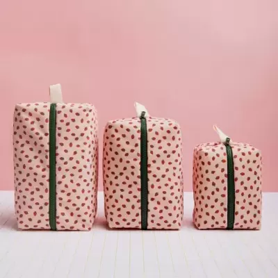 Três sacos de tecido cor-de-rosa com padrão vermelho, fechos éclair verticais e alças no topo