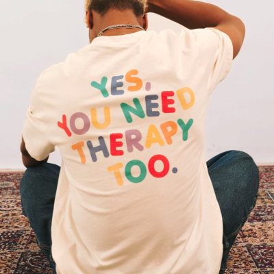 Pessoa de costas com t-shirt branca e texto colorido sentada num tapete padrão oriental