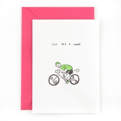 Cartão branco com ilustração de ciclista verde e texto You Are A Winner, sobre envelope vermelho.