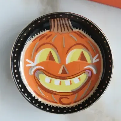 Prato redondo de cerâmica com desenho de abóbora sorridente e padrão de pontos na borda.