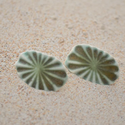 Brincos ovais verdes com padrão de linhas sobre areia