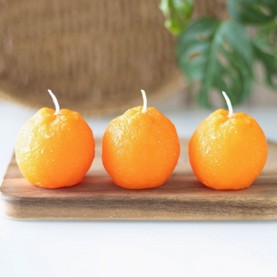 Três velas laranja em forma de fruta sobre tábua de madeira