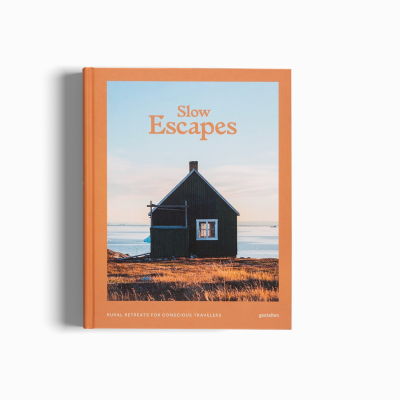 Capa de livro com casa preta à beira-mar, título 'Slow Escapes' em laranja