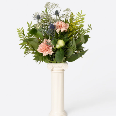 Arranjo floral com flores cor-de-rosa e folhagem verde num vaso branco tipo coluna