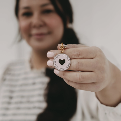 Chaveiro metálico prateado com coração e inscrições, segurado por uma mão