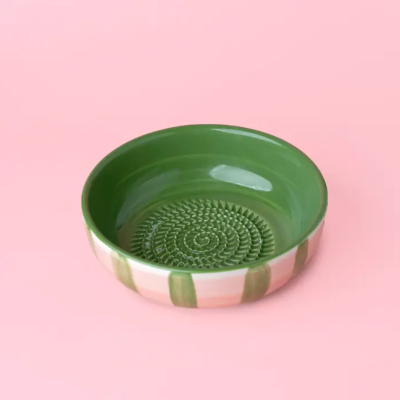 Tigela verde com padrão texturizado interior, riscas verticais no exterior, em fundo rosa.