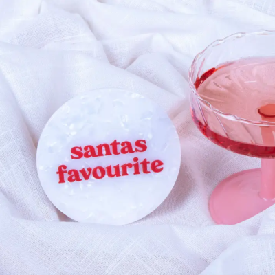 Porta-copos branco com texto vermelho e copo rosa com bebida cor-de-rosa sobre tecido branco