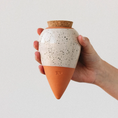 Mão segura vaso cerâmico bicolor com tampa de cortiça.