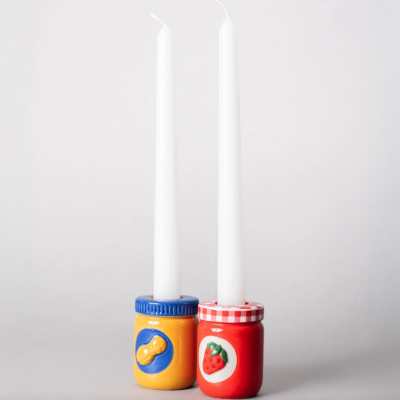 Velas brancas em suportes cerâmicos coloridos com desenhos de amendoim e morango.