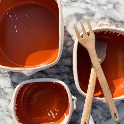 Três taças de cerâmica creme com interior laranja e talheres de madeira numa superfície de mármore cinzento e branco.