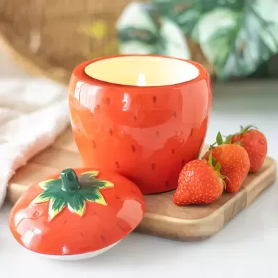 Vela em frasco cerâmico decorativo em forma de morango com tampa e morangos ao lado