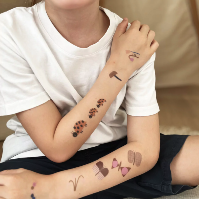 Criança com tatuagens temporárias nos braços sentada em interior com sofá bege