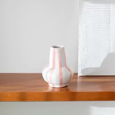 Vaso de cerâmica riscado em branco, rosa e verde sobre mesa de madeira