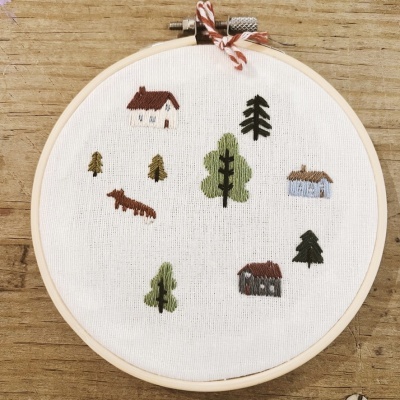 Aro de bordado com tecido branco e pequenos bordados de casas e árvores coloridas