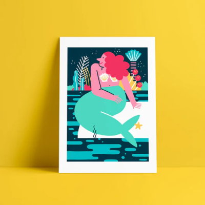 Ilustração colorida de sereia sentada numa pedra com fundo marinho, em moldura branca contra parede amarela