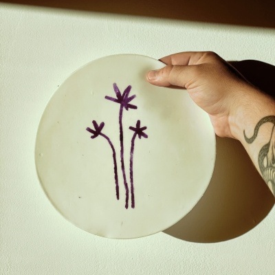 Prato branco com flores roxas e mão tatuada segurando