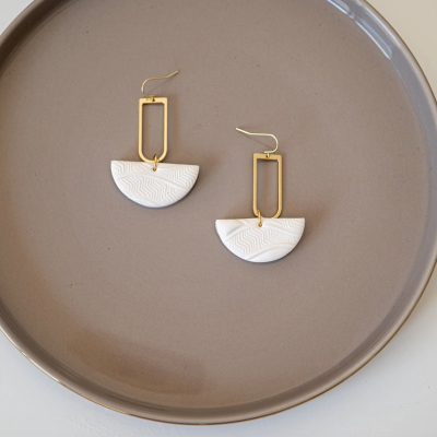 Brincos dourados e brancos com padrão ondulado sobre base cinza