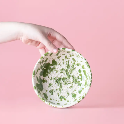 Prato redondo em cerâmica branca com manchas verdes e fundo rosa