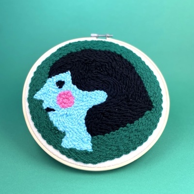 Bordado em bastidor circular com rosto feminino azul e cabelo preto