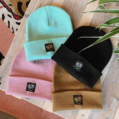 Quatro gorros de malha em azul claro, preto, rosa e castanho com etiquetas pretas e douradas