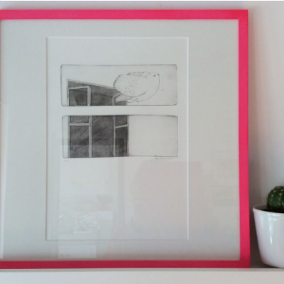 Moldura rosa com gravura monocromática e vaso branco com cacto