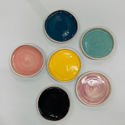 Seis pequenos pratos cerâmicos coloridos com esmalte brilhante em seis cores diferentes, sobre superfície branca