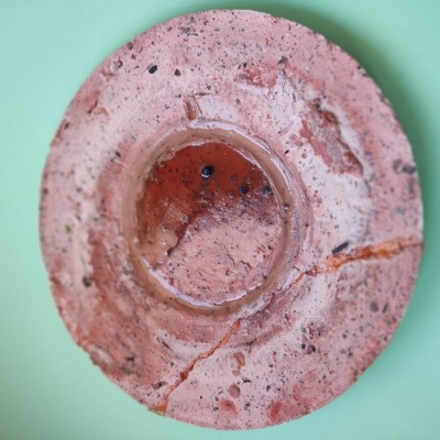Prato redondo rosa de cerâmica com fissuras sobre fundo verde claro