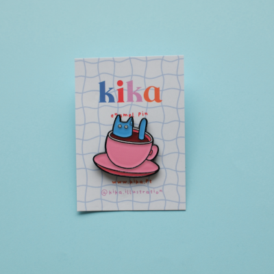 Pin esmaltado de gato azul dentro de chávena rosa em cartolina com texto kika e padrão azul