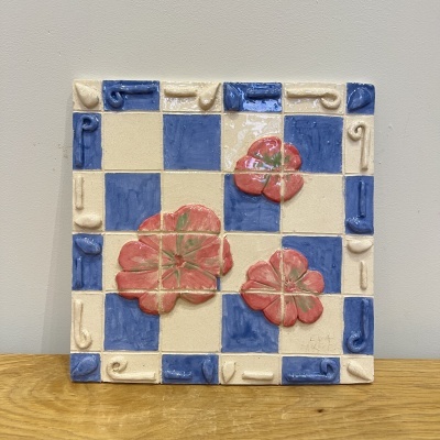 Azulejo cerâmico decorativo com padrão quadriculado azul e creme com flores vermelhas e relevo nas bordas