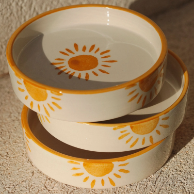 Três tigelas de cerâmica com desenho de sol amarelo e laranja, empilhadas sobre superfície clara