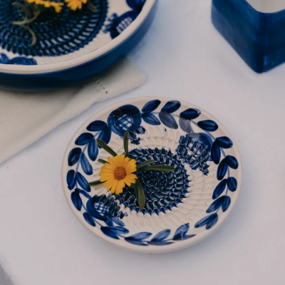Conjunto de loiça azul e branca com padrão floral e flor amarela sobre uma mesa branca.