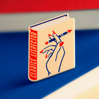 Broche esmaltado com design de livro e mão a segurar caneta