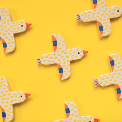 Pássaros decorativos de madeira amarelos com pintas azuis e laranja sobre fundo amarelo