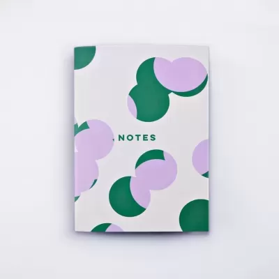 Caderno branco com padrões verdes e cor-de-rosa e a palavra NOTES na capa