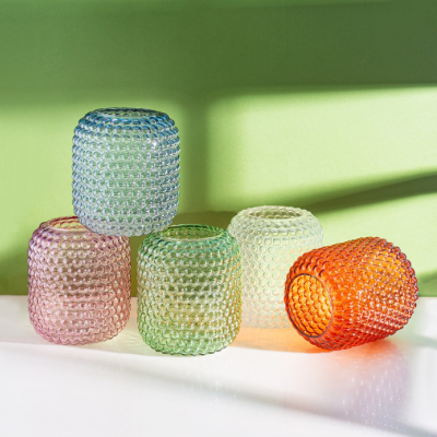 Cinco copos de vidro coloridos com textura em relevo tipo bolhas em fundo verde