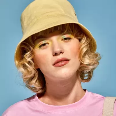 Pessoa com chapéu bucket amarelo e t-shirt rosa sobre fundo azul claro